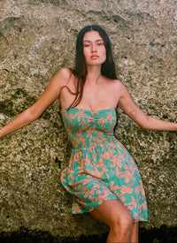 Woman in a floral dress leaning against a textured stone wall